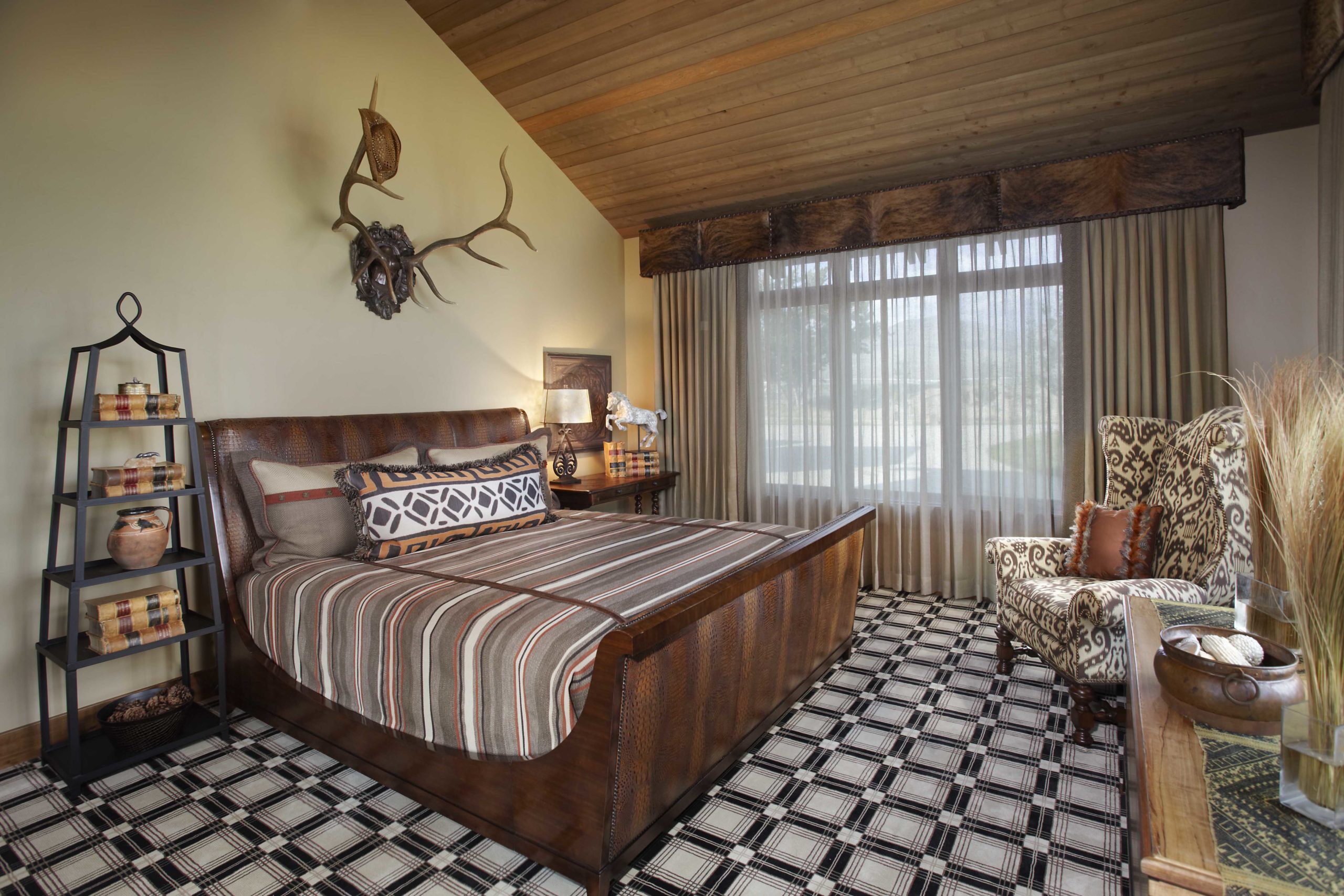 Bedroom with plaid carpet, a dark wooden and leather bed frame and antlers hanging above the bed