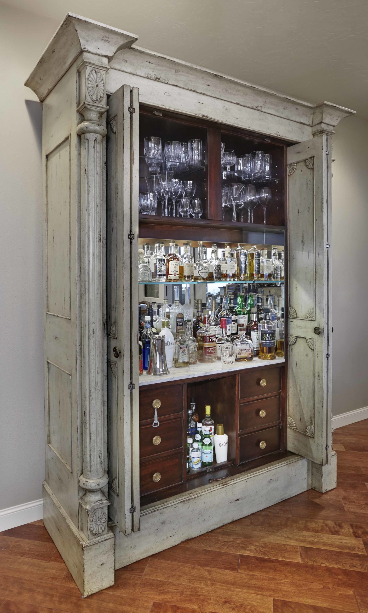 Furniture piece that opens to be a bar car with glasses and dozens of liquor bottles on the shelves