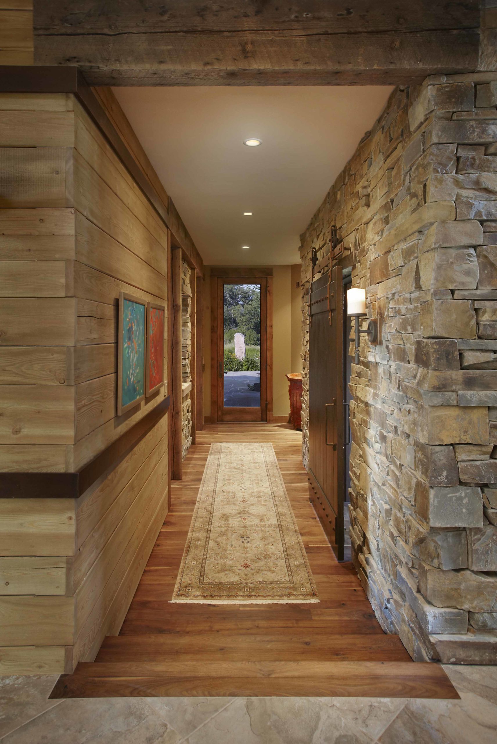 Hallway with one wood paneled wall, one stone wall and a long Persian runner on the wooden floors